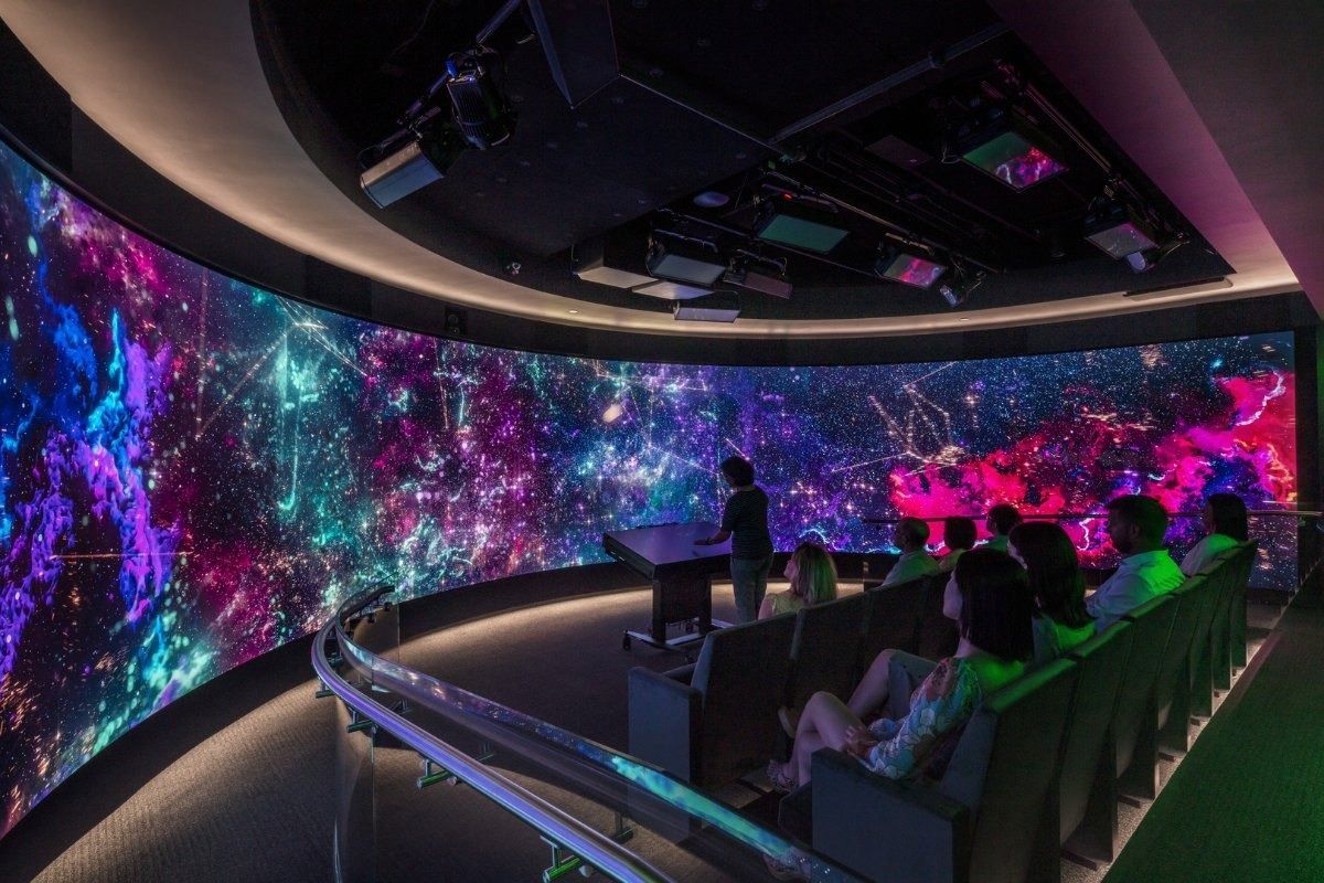 Hewlett Packard Enterprise: Dark room with a large curved wraparound screen showing a colourful space image and rows of seats