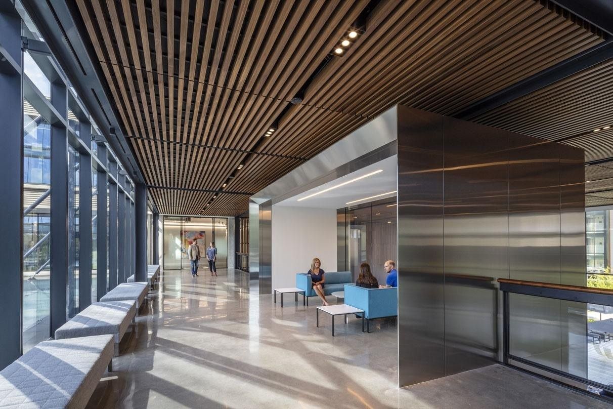 Hewlett Packard Enterprise: Glass-walled corridor with a wood-slat ceiling, built-in benches and a stainless-steel clad seating nook