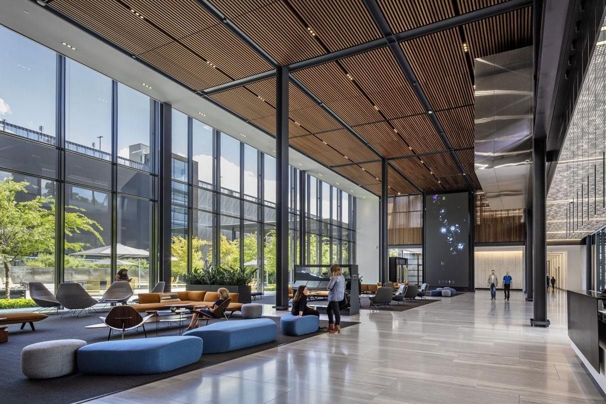 Hewlett Packard Enterprise: Tall glass lobby with a wood-slat ceiling, blue and grey lounge seating and a large video wall