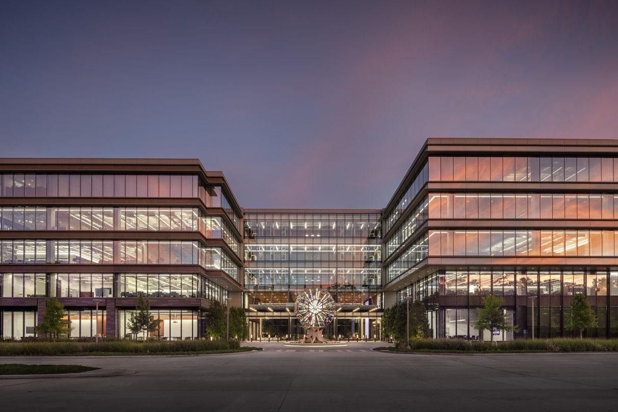 Two glass office buildings at dusk framing a lit entrance and a large spherical sculpture