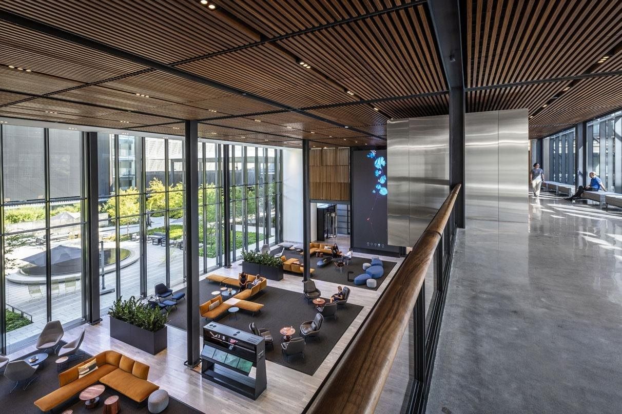 Hewlett Packard Enterprise: View from an upper walkway down onto a lounge with orange sofas beside full-height windows