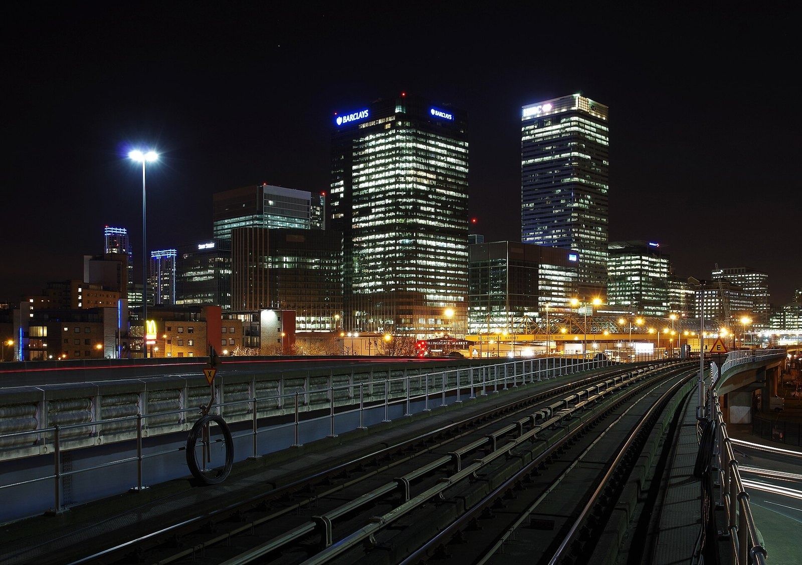 HSBC: Lit office towers at night seen along elevated railway tracks