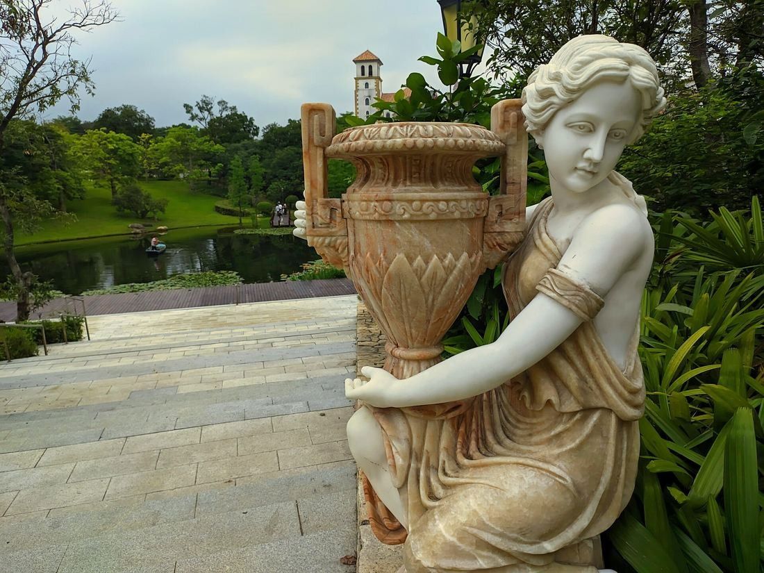 Huawei: Classical stone statue holding an urn beside steps, lake and greenery behind