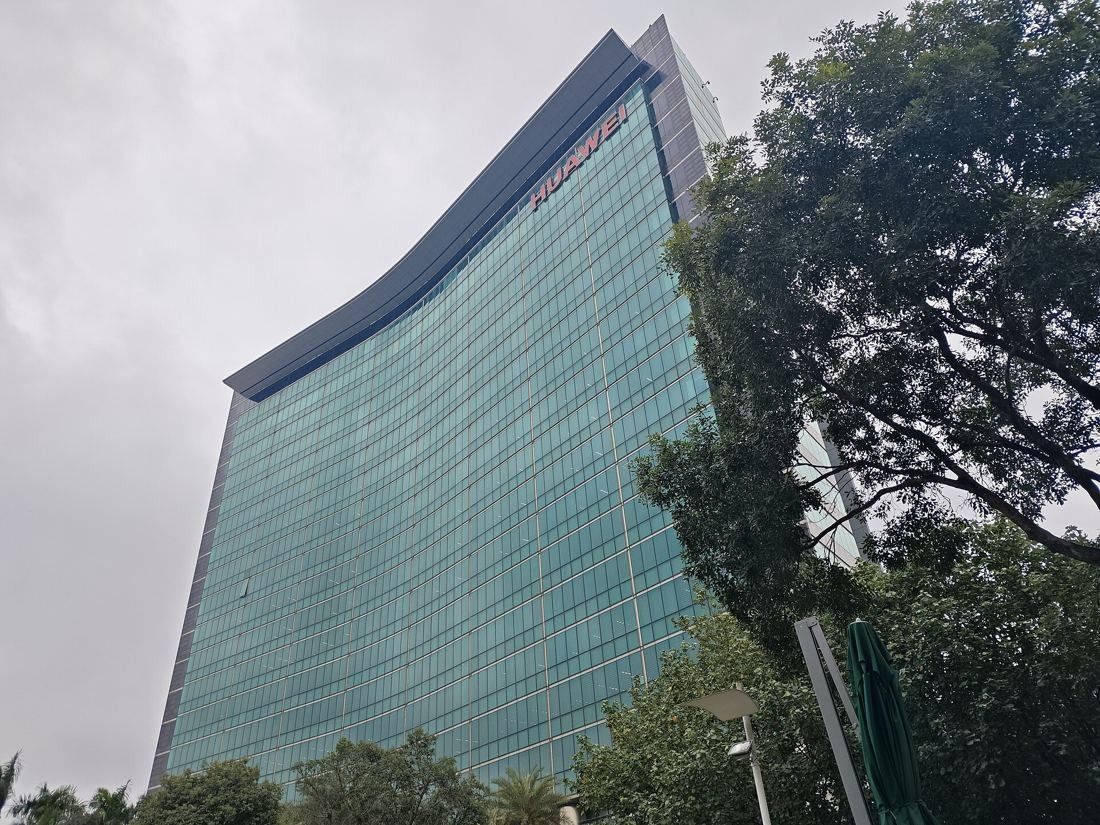 Huawei: Curved glass office tower seen from below, framed by trees under a cloudy sky
