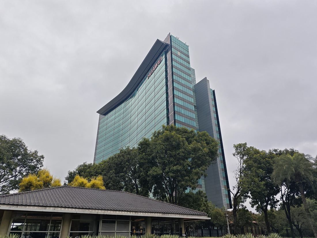 Huawei: Curved glass tower rising behind trees and a low pavilion roof