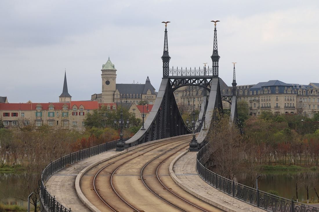 Huawei: Curving tram tracks leading onto an iron bridge with spires, European-style buildings behind