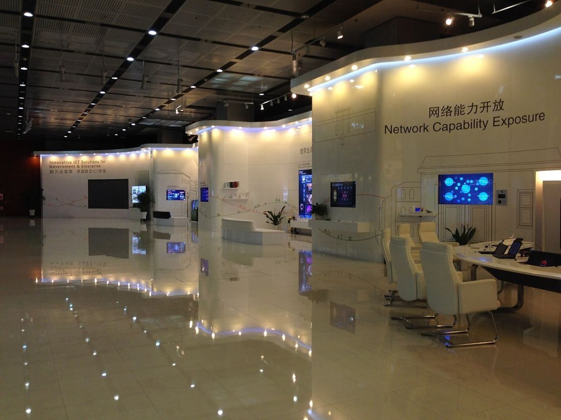 Huawei: Glossy exhibition hall with curved white walls, screens and white chairs at a round table