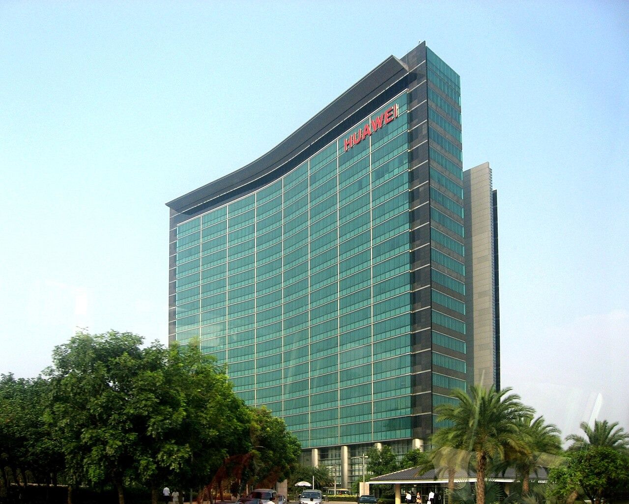 Curved glass Huawei office tower behind palm trees in Bantian