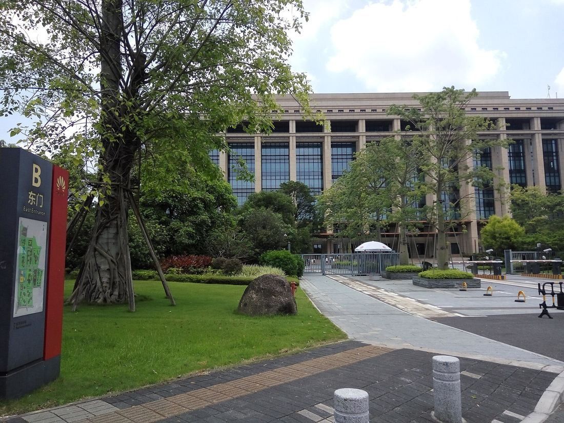 Huawei: Large stone office building behind lawns, trees and a zone sign