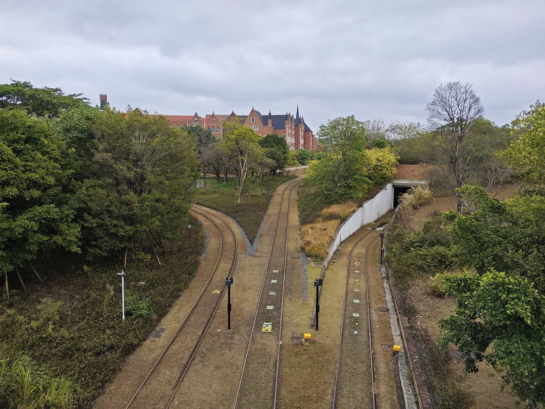 Huawei: Railway tracks curving between trees toward red-roofed buildings