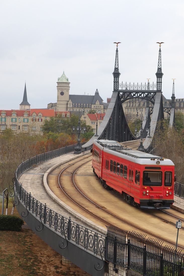 Huawei: Red tram crossing a curved iron bridge with Gothic spires