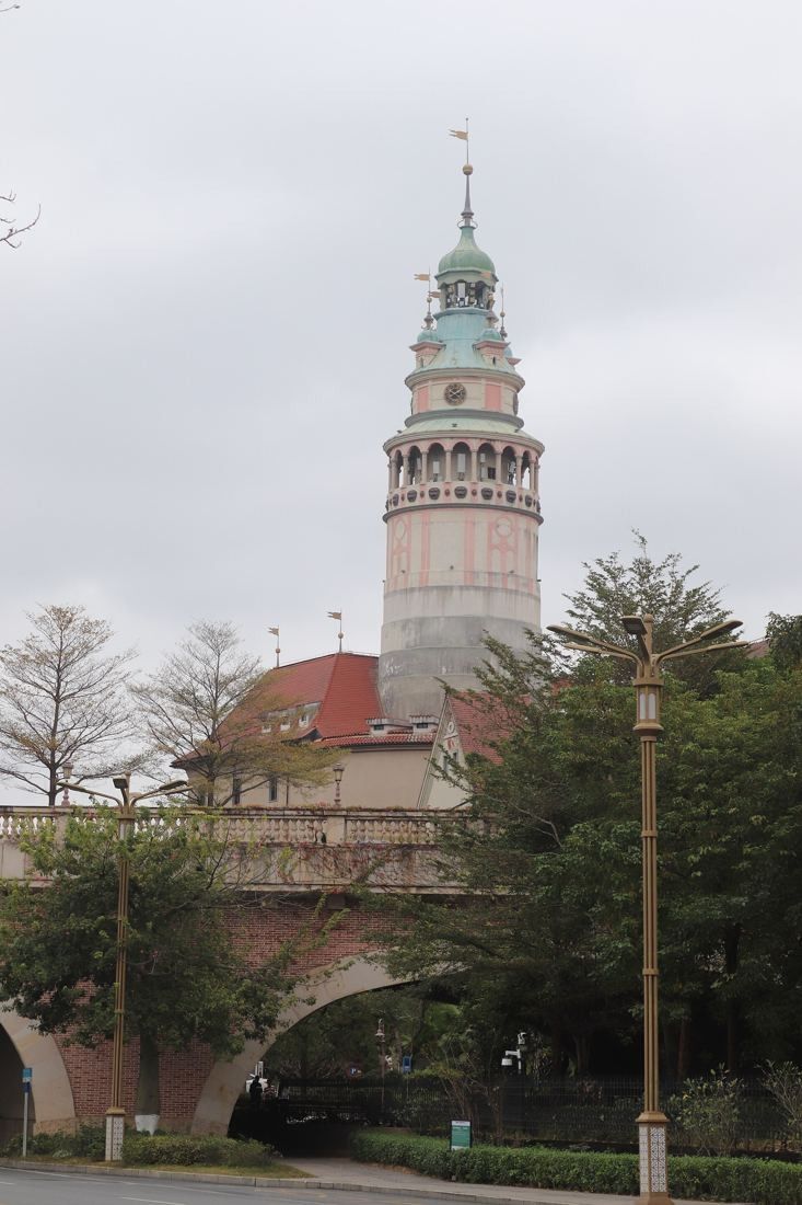 Huawei: Slender lighthouse-like tower above a stone arch bridge and trees