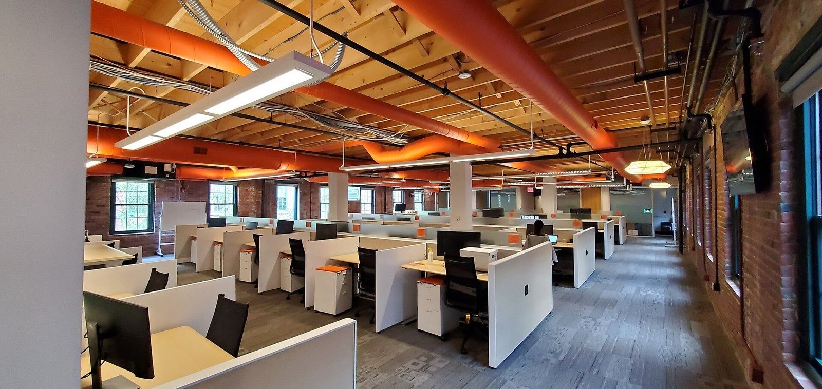 HubSpot: Open desks under timber beams and orange ducts in a brick mill building