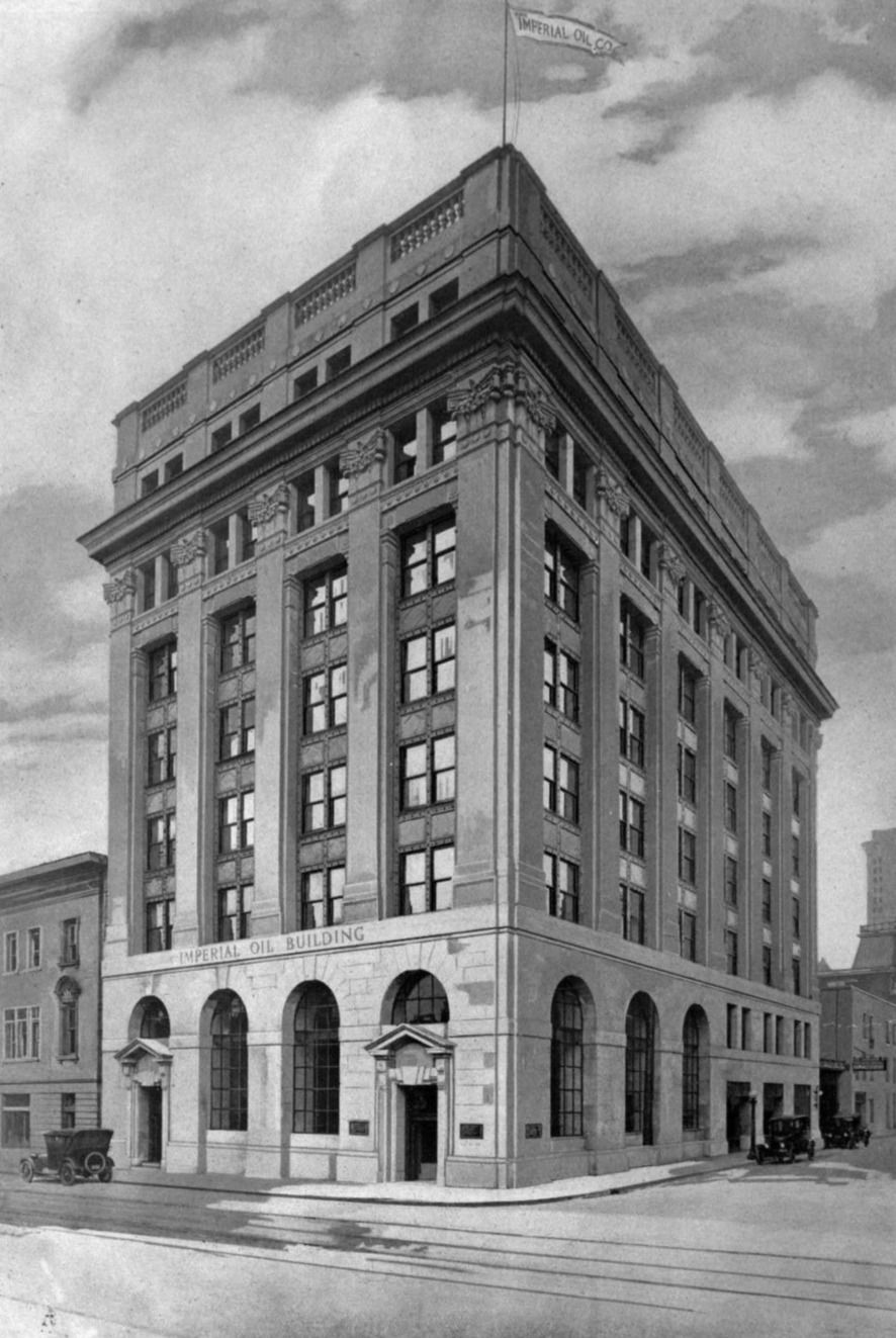 A black-and-white photograph of a seven-storey stone office building on a street corner with old cars outside