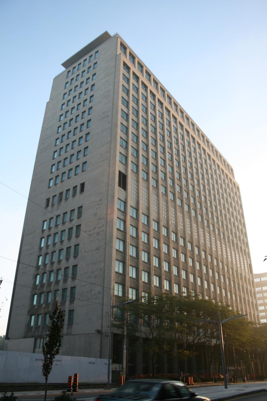 A tall pale stone office tower with rows of small windows above trees