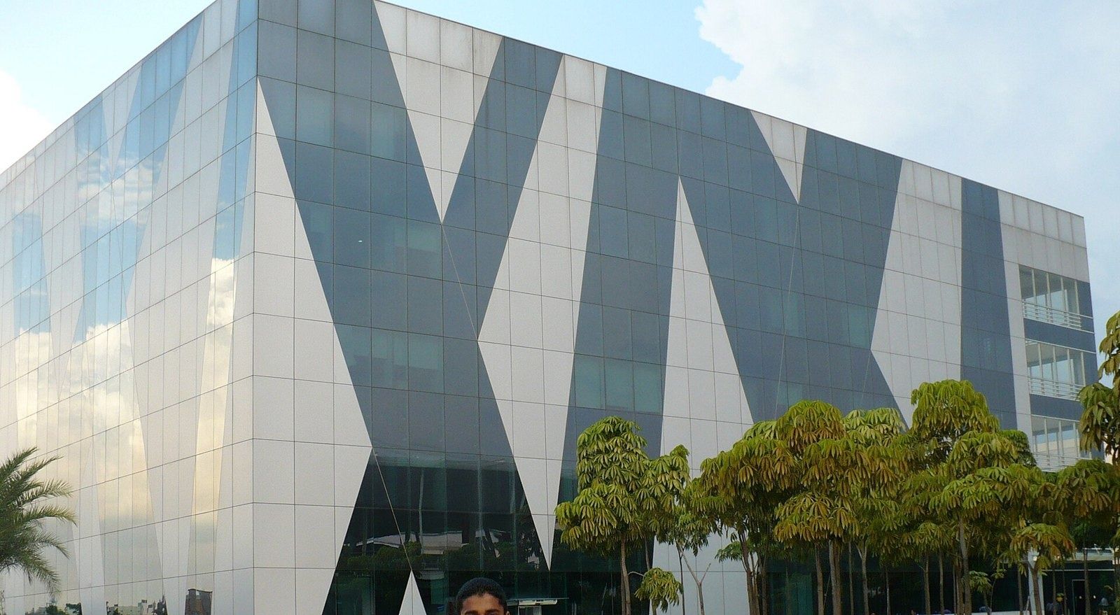 Infosys: Glass facade with large angular grey pattern, trees in front