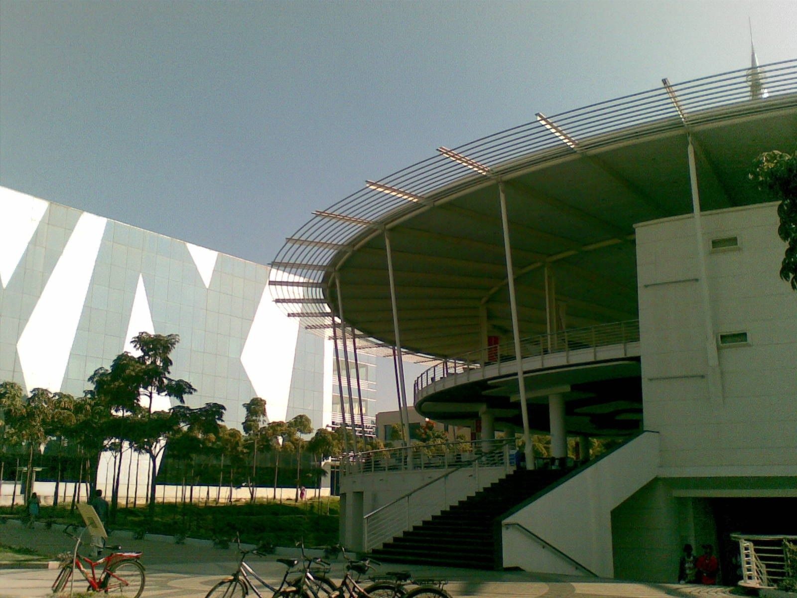 Infosys: Round building with a ringed canopy beside a glass facade, bicycles parked outside