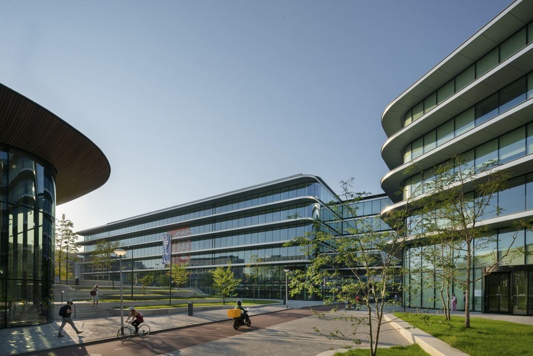 Curved glass office wings with horizontal white bands around a landscaped plaza under a clear sky