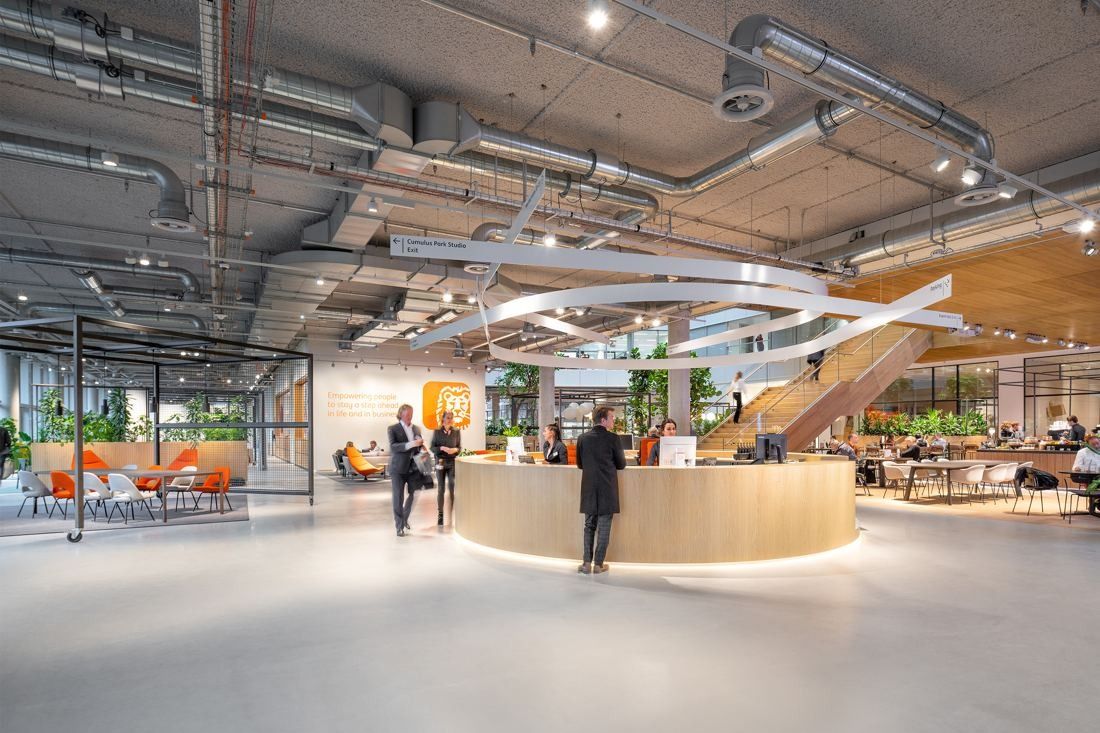 ING Group: Ground-floor lobby with a round wooden reception desk, exposed ducts and a curved white light sculpture