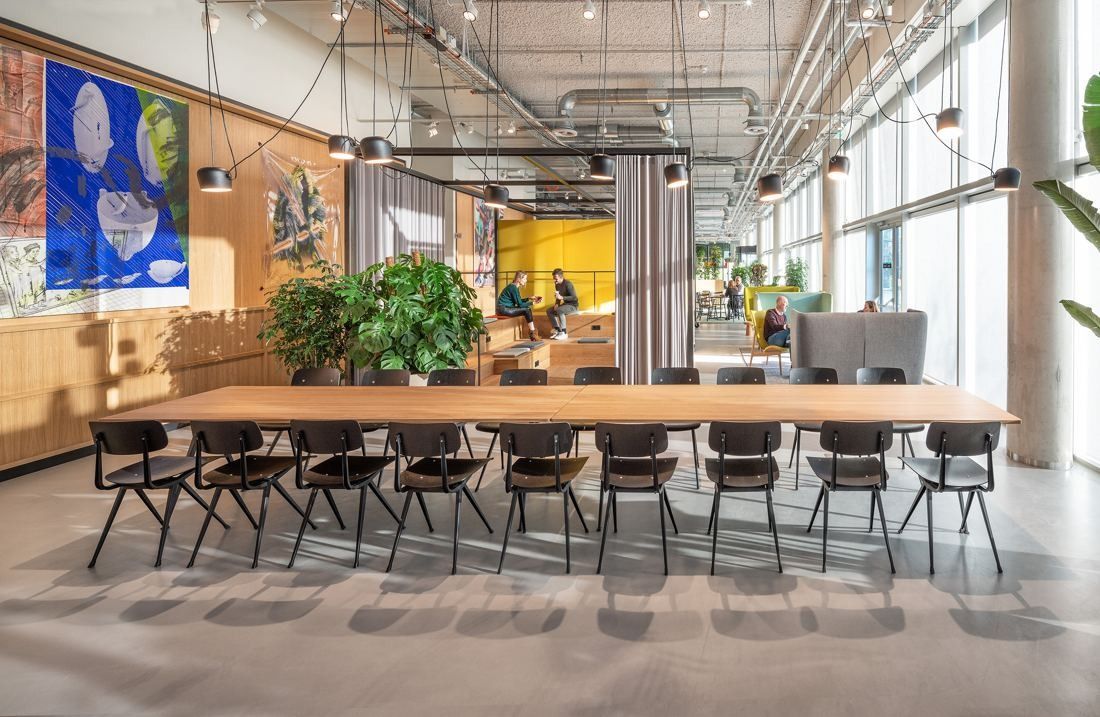 ING Group: Long wooden table with black chairs under pendant lights, plants and colourful artworks