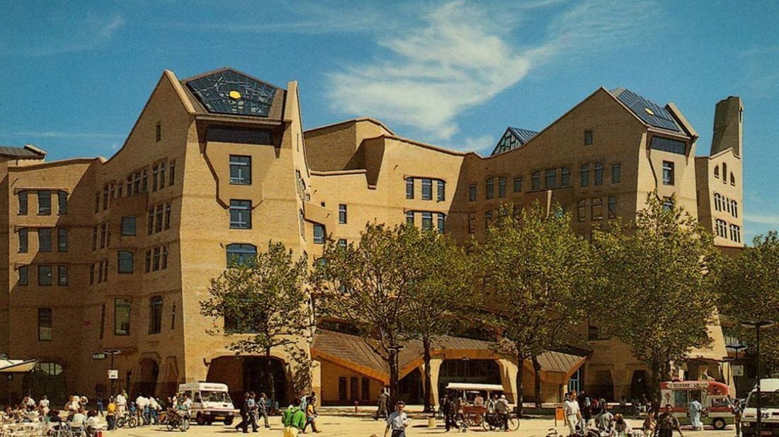 Organic brick office complex with sloping roofs and tree-lined square in front