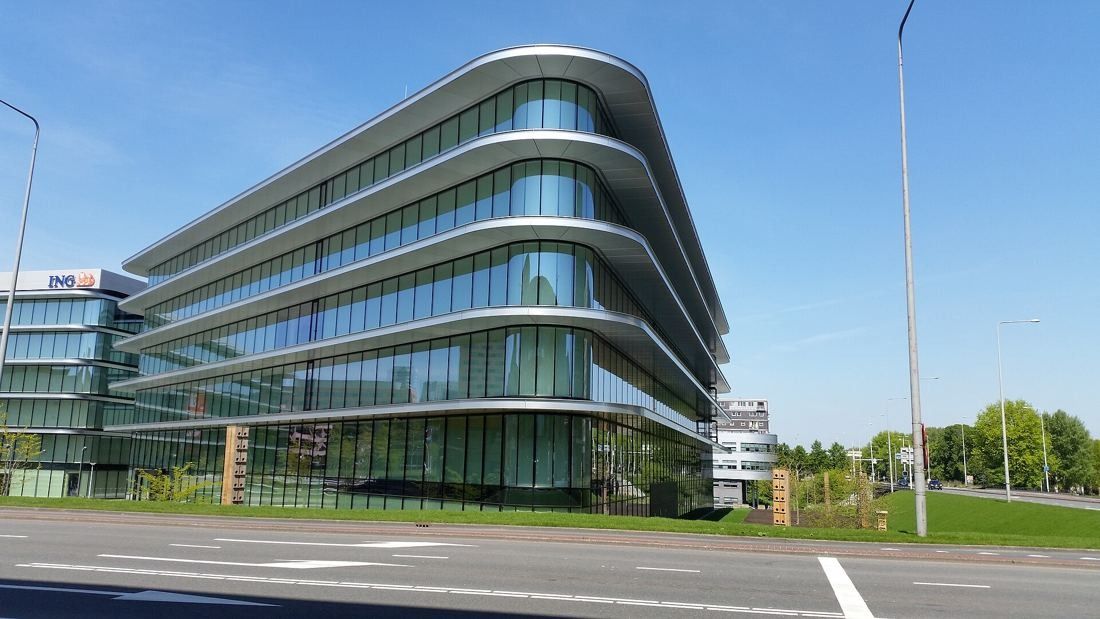 ING Group: Rounded glass building corner seen from across a road under a blue sky
