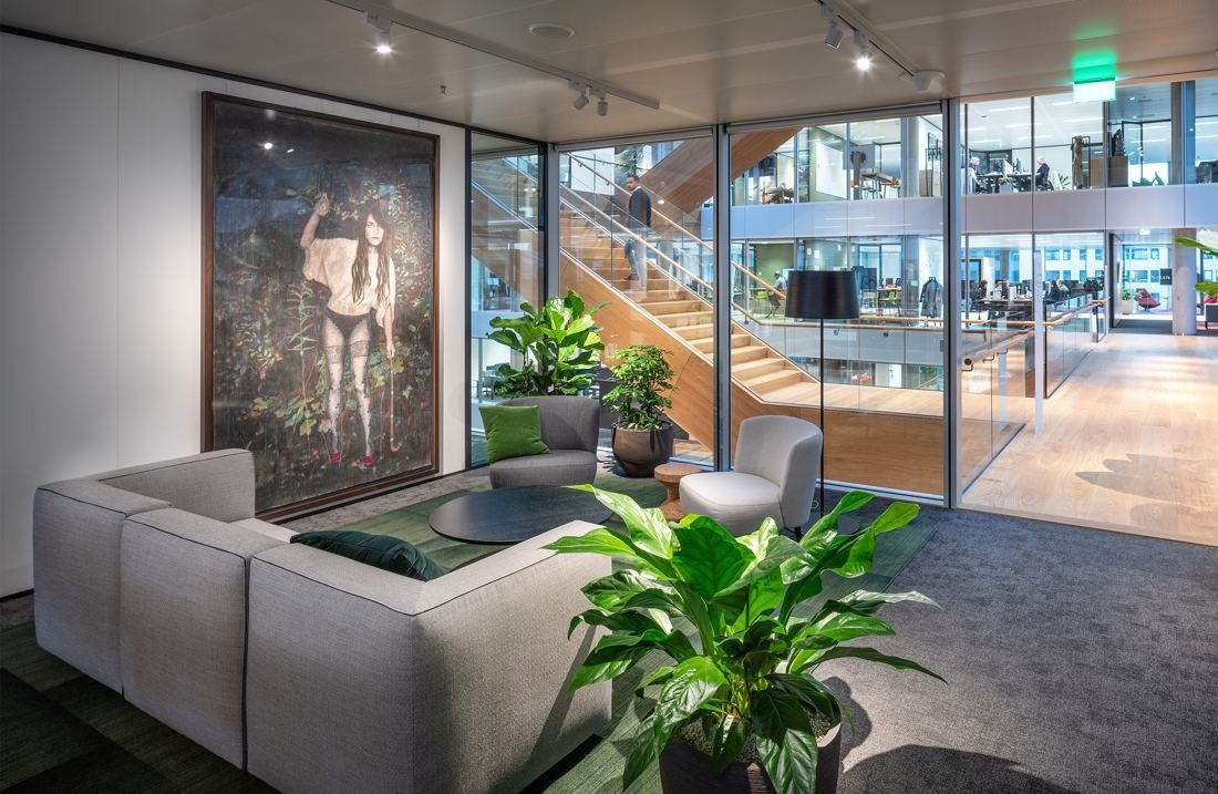 ING Group: Seating corner with a grey sofa, plants and a large dark painting by a glass wall