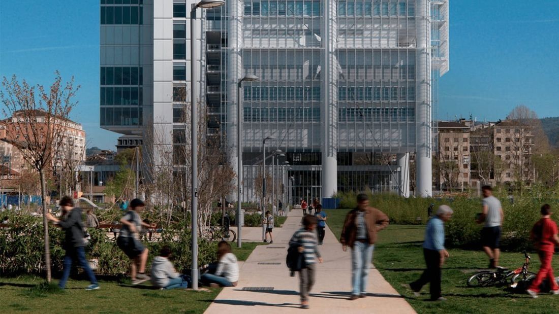 Intesa Sanpaolo: Glass tower base behind a public garden with a path, lawns and passers-by