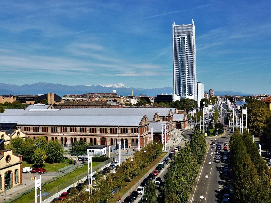 Intesa Sanpaolo: The tower rising beyond a tree-lined avenue and low brick buildings, with mountains on the horizon