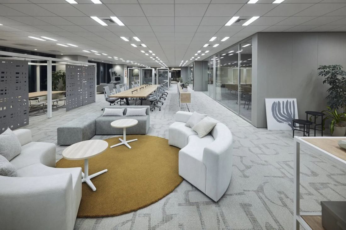 ITOKI: Curved white sofas on a round mustard rug with work tables beyond