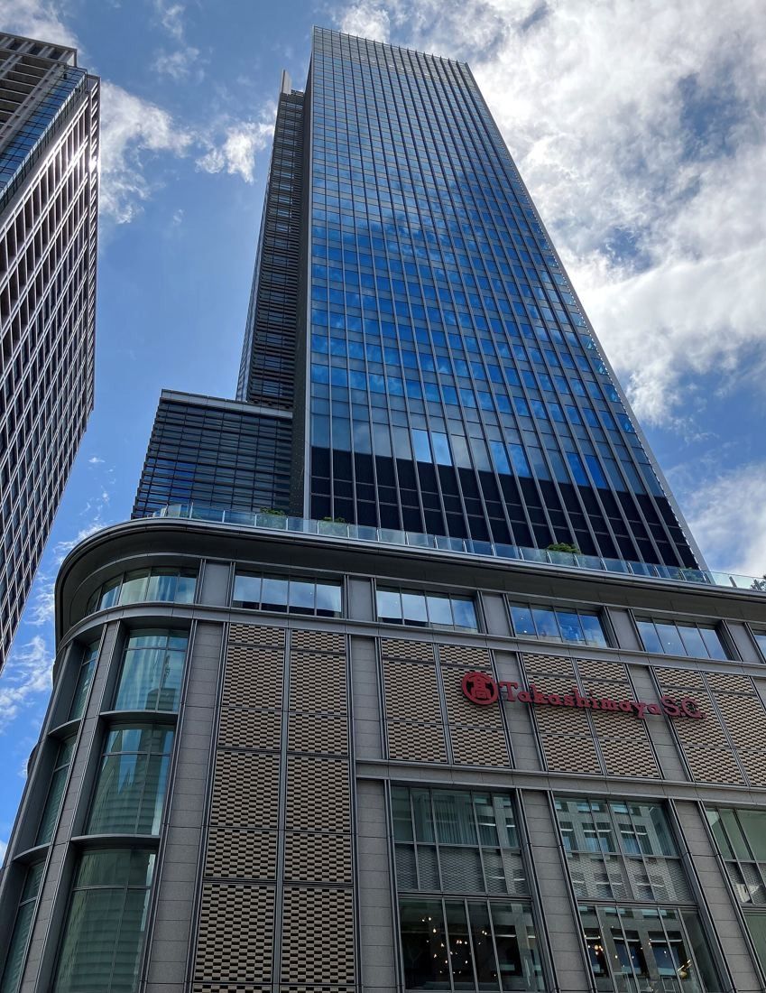 ITOKI: Glass office tower rising above a stone-clad lower block, seen from the street