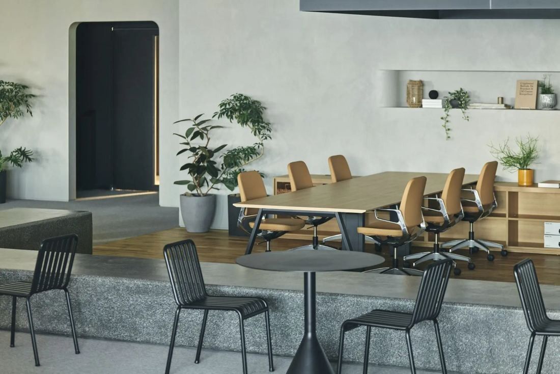 ITOKI: Meeting table with orange chairs beside a raised concrete step and plants
