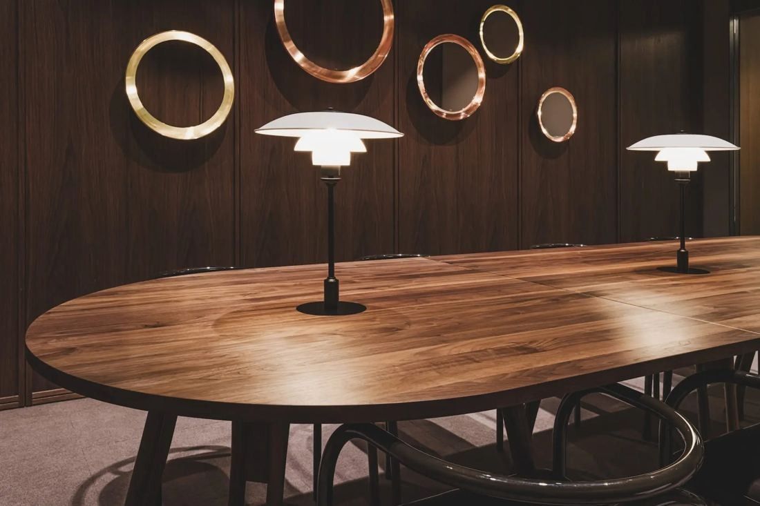 ITOKI: Oval wooden table under lamps with brass ring mirrors on the wall