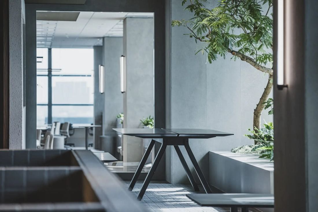 ITOKI: Table and chairs by a planted area with windows to the city