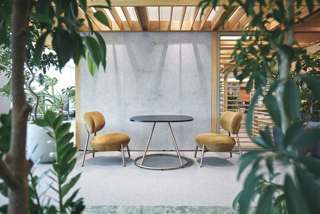 ITOKI: Two yellow armchairs and a round table framed by plants and timber slats