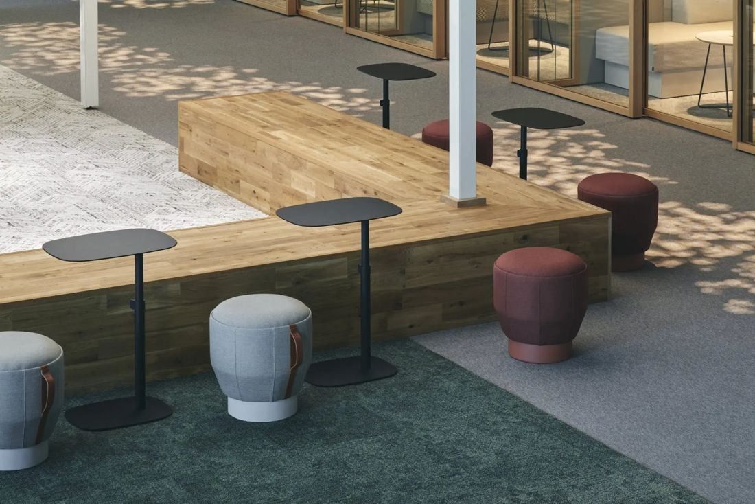 ITOKI: Wooden platform with stools and high tables on a patterned carpet