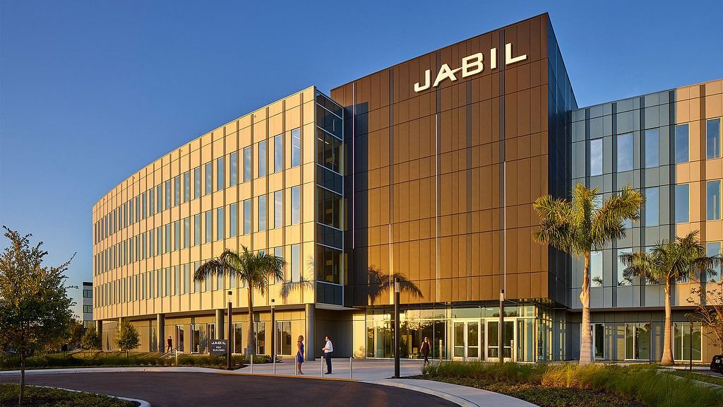 A golden-glass office building with a large JABIL sign, palm trees and a curving drive at sunset
