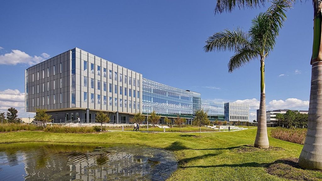 Jabil: A low glass office building beyond a pond and grassland with palm trees
