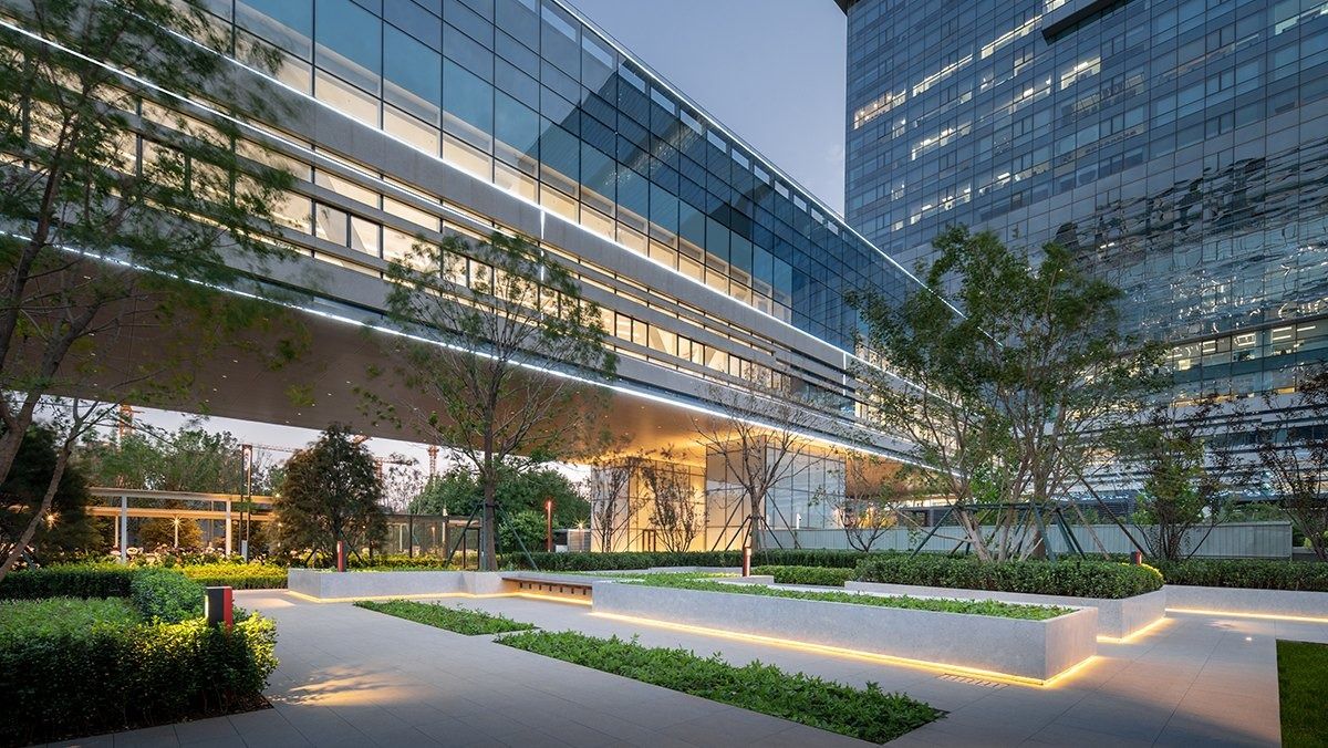 JD.com: Glass office wing over a lit garden walkway at dusk