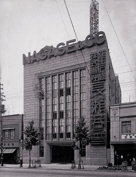 A black-and-white photo of a multi-storey stone-faced building with a vertical sign and NAGASE & CO lettering