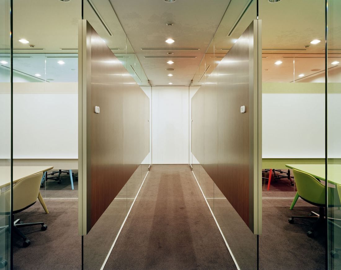 Kao: A glass-walled corridor between meeting rooms with a wood floor