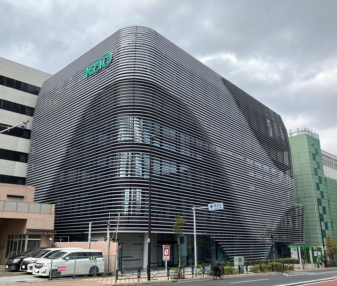 A modern office building with a curved, horizontally ribbed silver façade and a green Kao sign