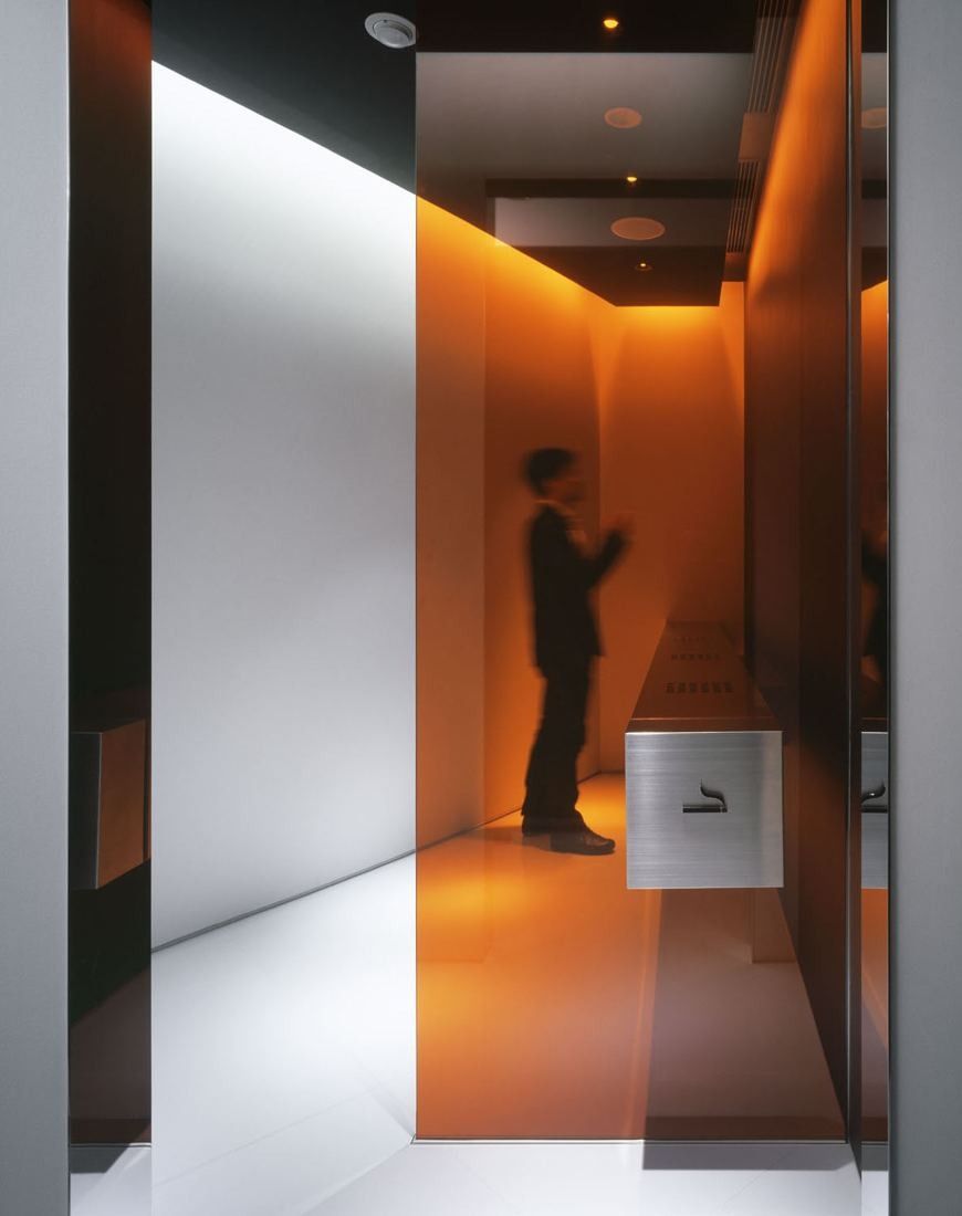 Kao: A narrow corridor lit in orange behind glass, with a motion-blurred figure