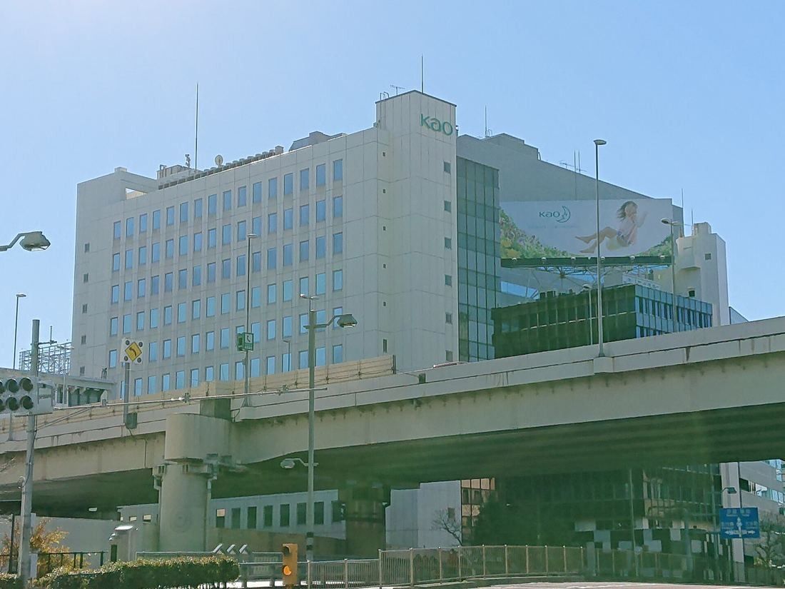 Kao: A pale multi-storey office building with a KAO sign on the roof, seen across an elevated expressway