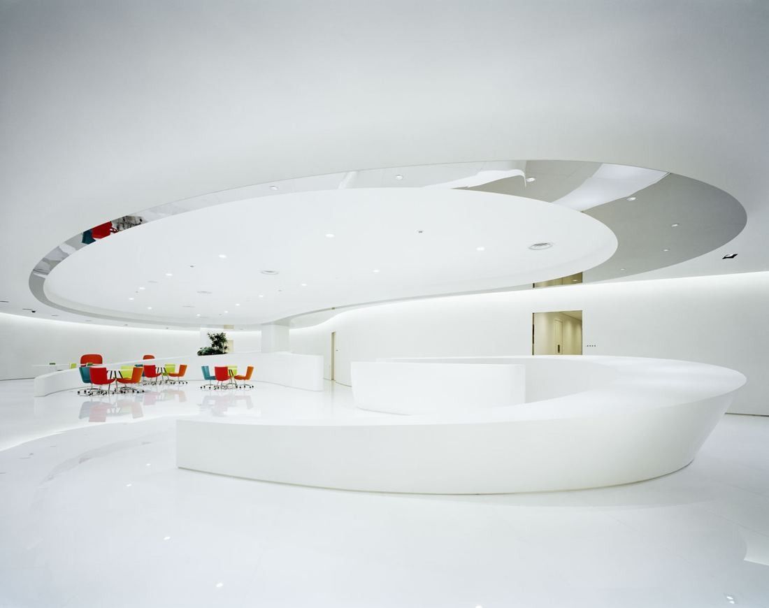 A seamless white lobby with curved counters and a domed ceiling, accented by small colourful chairs