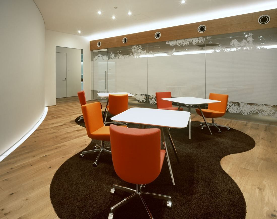 Kao: Orange chairs around white tables on a curved dark rug in a white room