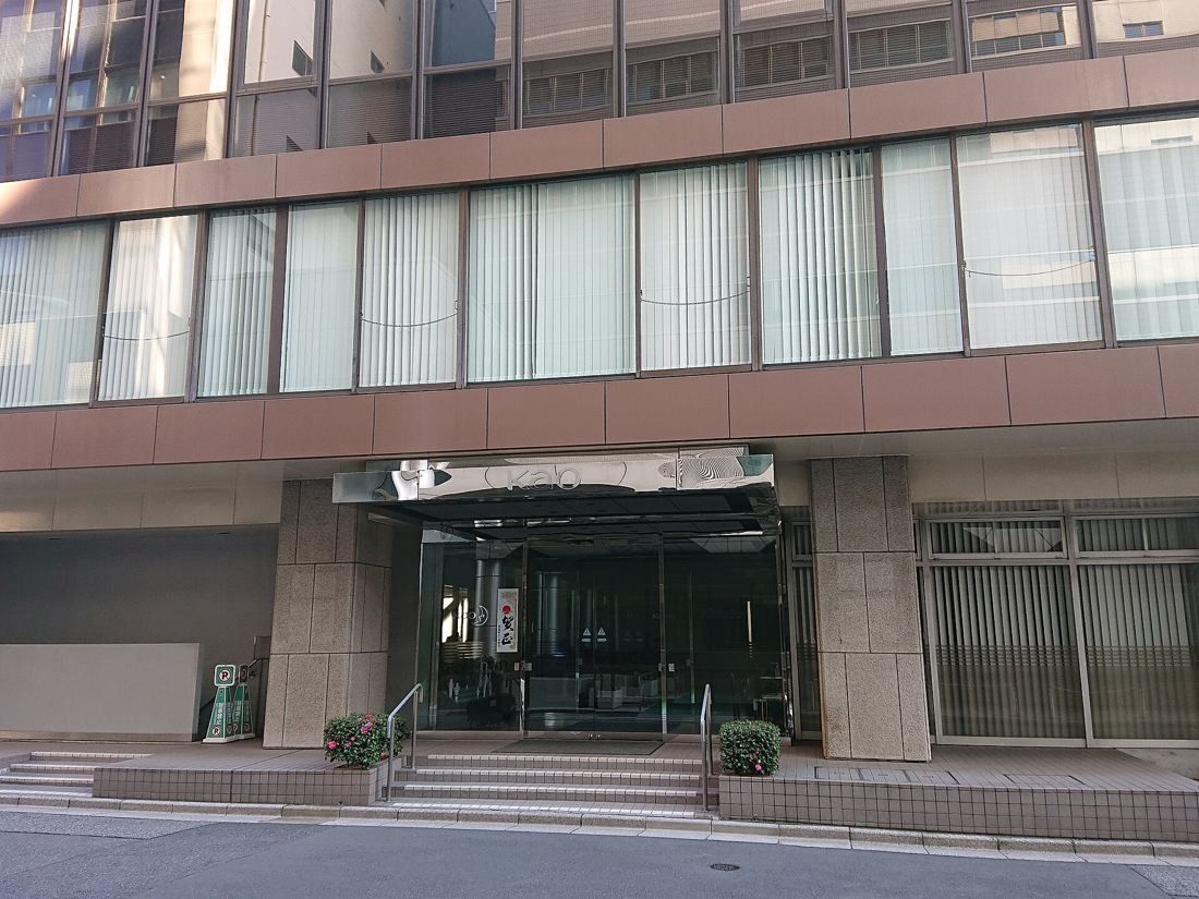 Kao: The covered ground-floor entrance of an office building with stone columns and glass doors