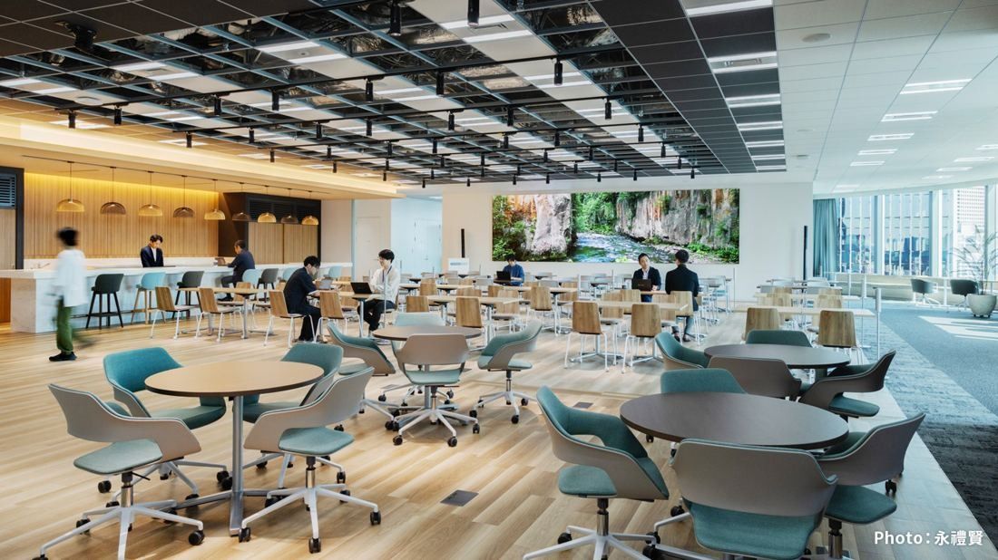 KDDI: A bright area with round tables, swivel chairs, a long counter and a large nature image on the wall