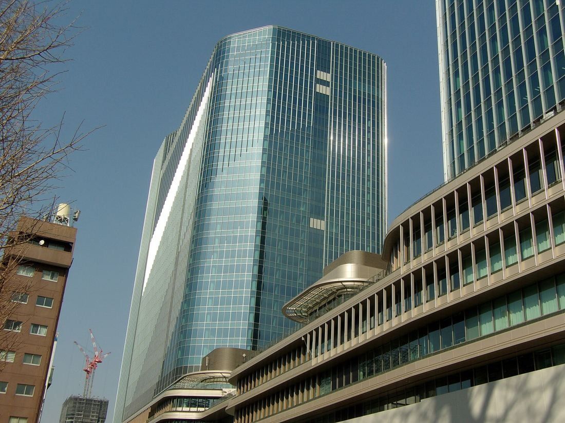 KDDI: A glass tower beside the curved terraces of a neighbouring podium on a sunny day