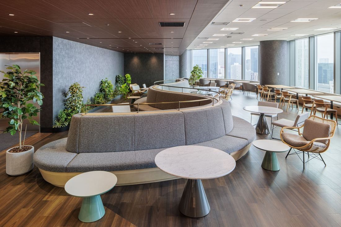 KDDI: A lounge with curved grey sofas, round white tables and plants beside tall windows
